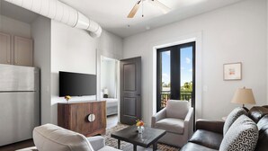Una sala de estar moderna con un sofá, sillones, una mesa de centro, un televisor y una puerta que da a un balcón exterior.