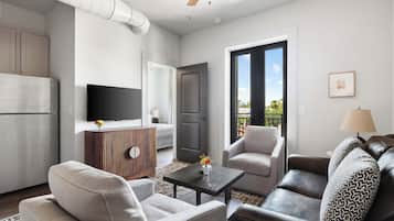 A modern living room with a sofa, armchairs, a coffee table, a TV, and a door leading to an outdoor balcony.