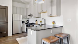 Une cuisine moderne avec des meubles blancs, un îlot central doté de tabourets, un luminaire suspendu doré et un réfrigérateur en acier inoxydable.