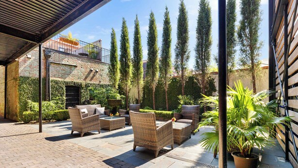An outdoor patio area with wicker furniture, potted plants, and a brick floor. - Fire Tower | Private 1BR King Suite + Rooftop View (Charleston)