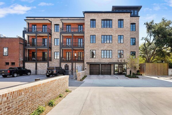 A multi-story residential building with a brick facade, balconies, and a garage. - Fire Tower | Charleston 1BR Condo + Rooftop Views (Charleston)