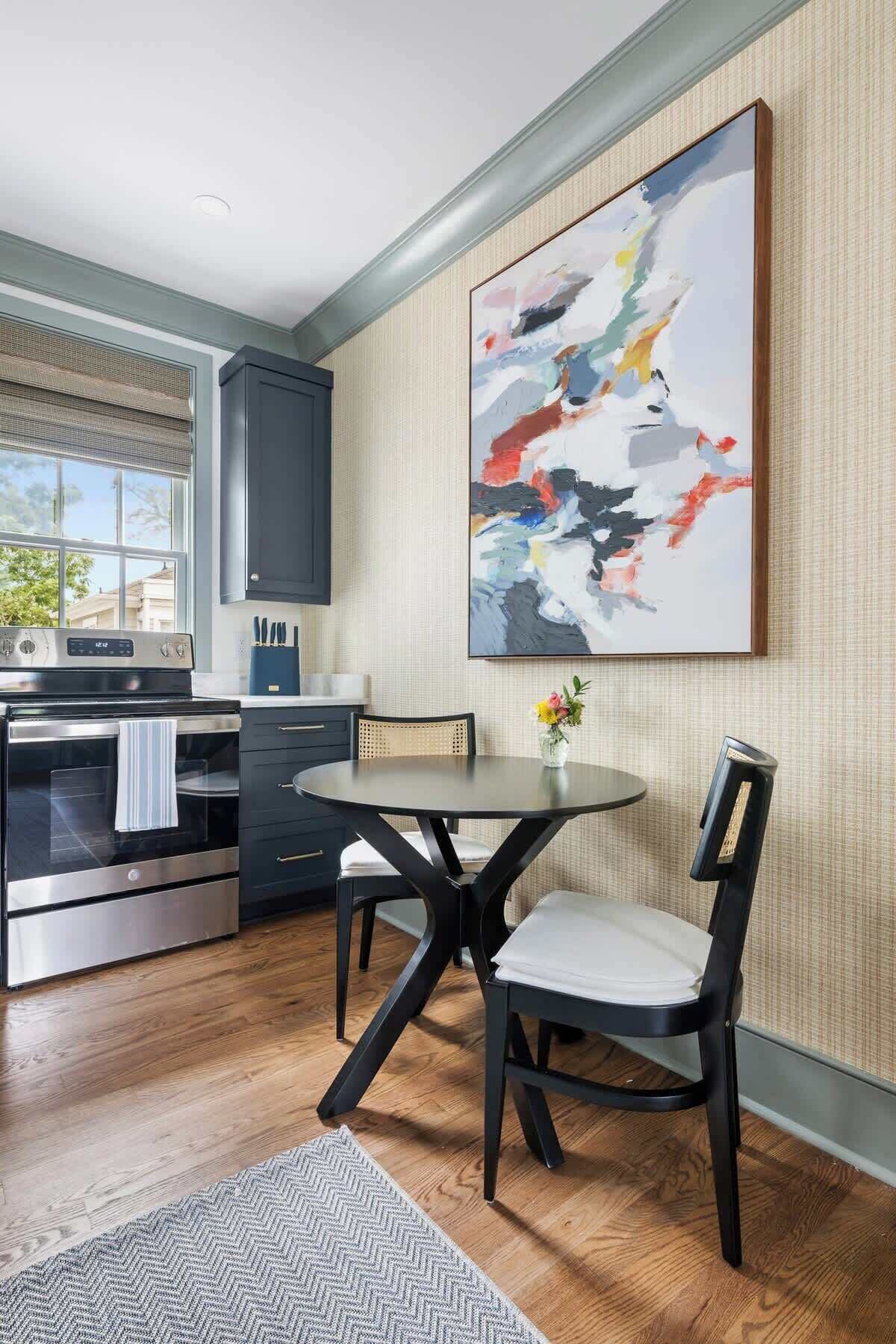 A modern kitchen with a large abstract painting, a dining table with chairs, and a view of the outside.