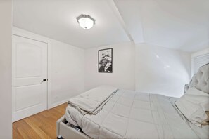 Une chambre à coucher avec un lit, une porte, un luminaire au plafond et un tableau encadré accroché au mur.