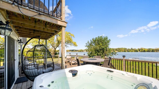 En træterrasse med jacuzzi, udendørs møbler og udsigt til et sø.
