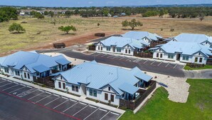 A row of single-story buildings with blue roofs, arranged in a linear fashion along a road. - Eagle's Villa 103 - Hot Tub, 5 Min to Main (Fredericksburg)