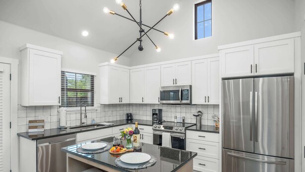 A modern kitchen with white cabinets, stainless steel appliances, a central island, and a pendant light fixture. - Eagle's Villa 103 - Hot Tub, 5 Min to Main (Fredericksburg)