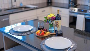 A kitchen counter with a wine bottle, a fruit platter, and a vase of flowers. - Eagle's Villa 103 - Hot Tub, 5 Min to Main (Fredericksburg)
