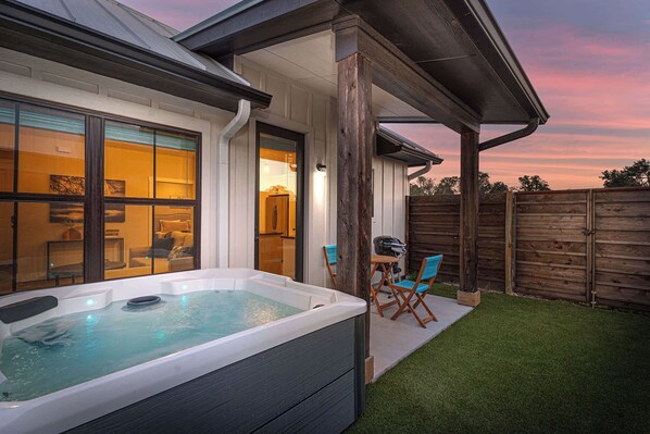 A hot tub in a backyard with a wooden deck, a wooden fence, and a grassy lawn.