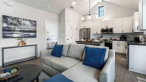 Eine moderne Küche mit weißen Schränken, Edelstahlgeräten und einem Essbereich mit grauem Sofa und blauen Kissen.