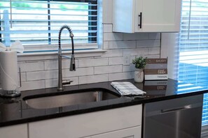 Uma cozinha com uma pia de aço inoxidável, uma janela com persianas e um armário sobre a pia.