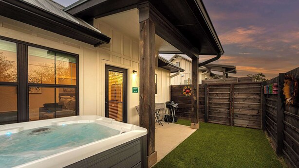 Een hottub in een achtertuin met een houten schutting, een terras en een huis met grote ramen.