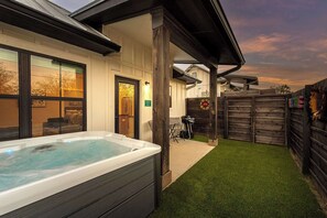 A hot tub in a backyard with a wooden fence, a patio, and a house with large windows. - Eagle's Hub 104 - Hot Tub, 5 Min to Main (Fredericksburg)