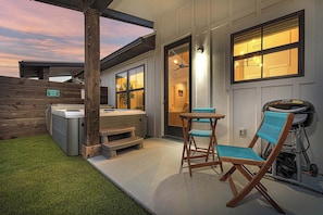 A patio with a hot tub, a wooden deck, and a chair.