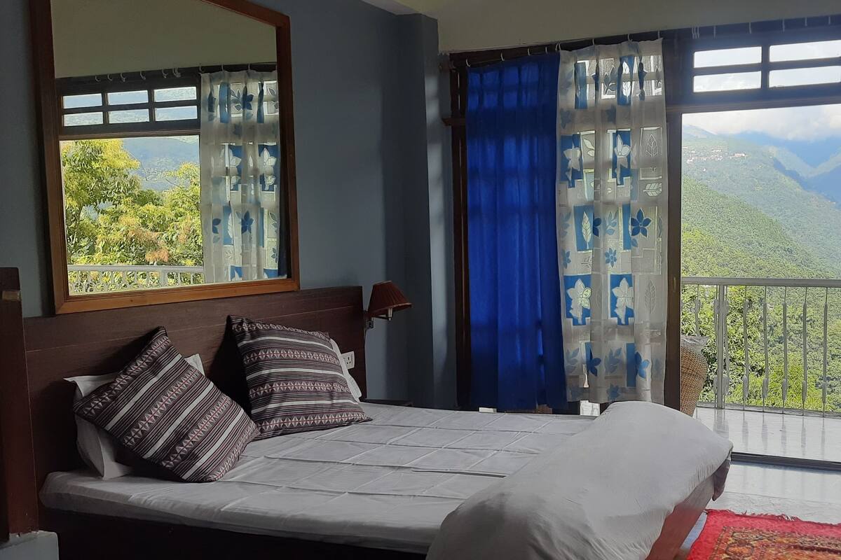 A bedroom with a bed, a nightstand, a lamp, and a view of mountains through the window.