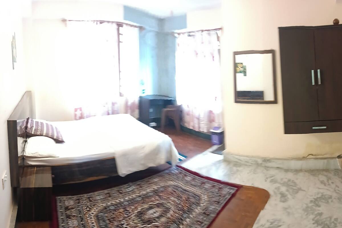 A bedroom with a bed, a wardrobe, a mirror, and a patterned rug.