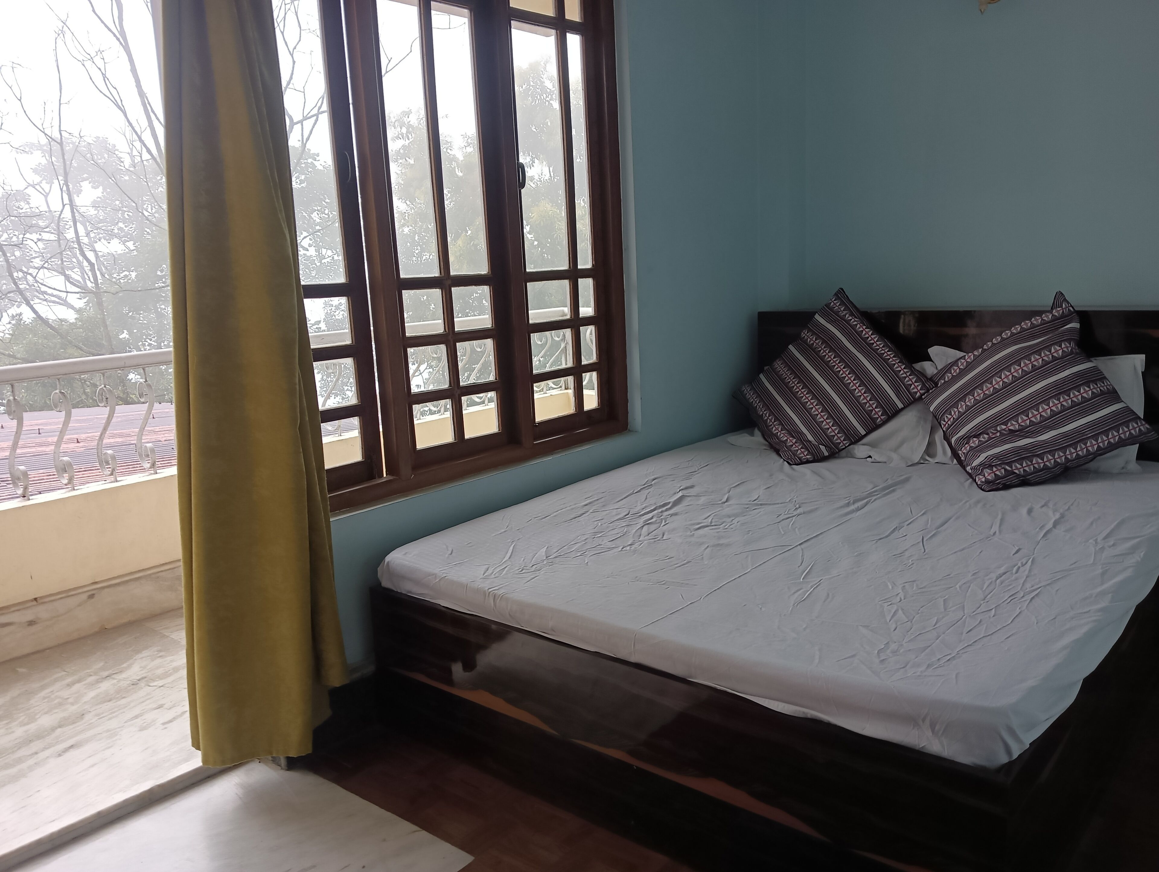Een slaapkamer met een bed, een raam met uitzicht op bomen en een balkon.