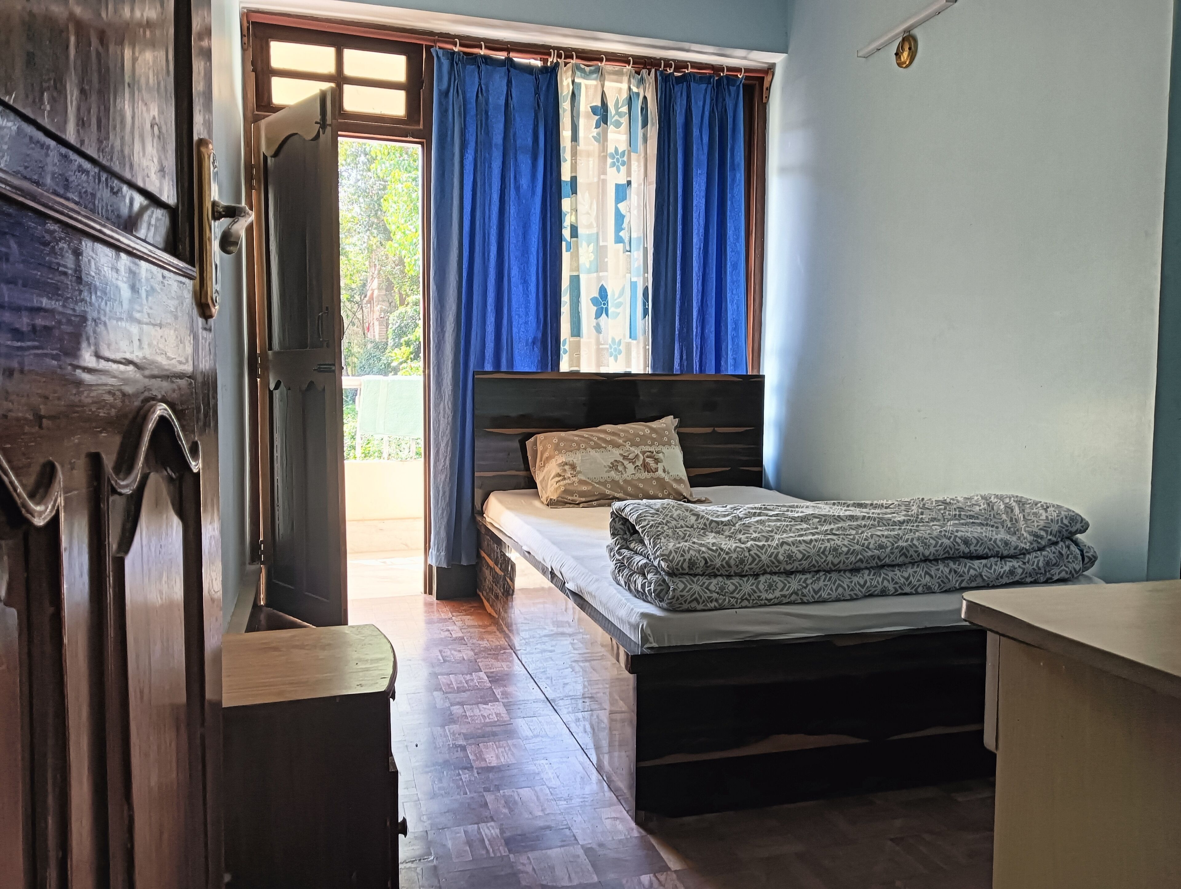 Un dormitorio con cama y cómoda de madera, y una ventana con cortinas azules.