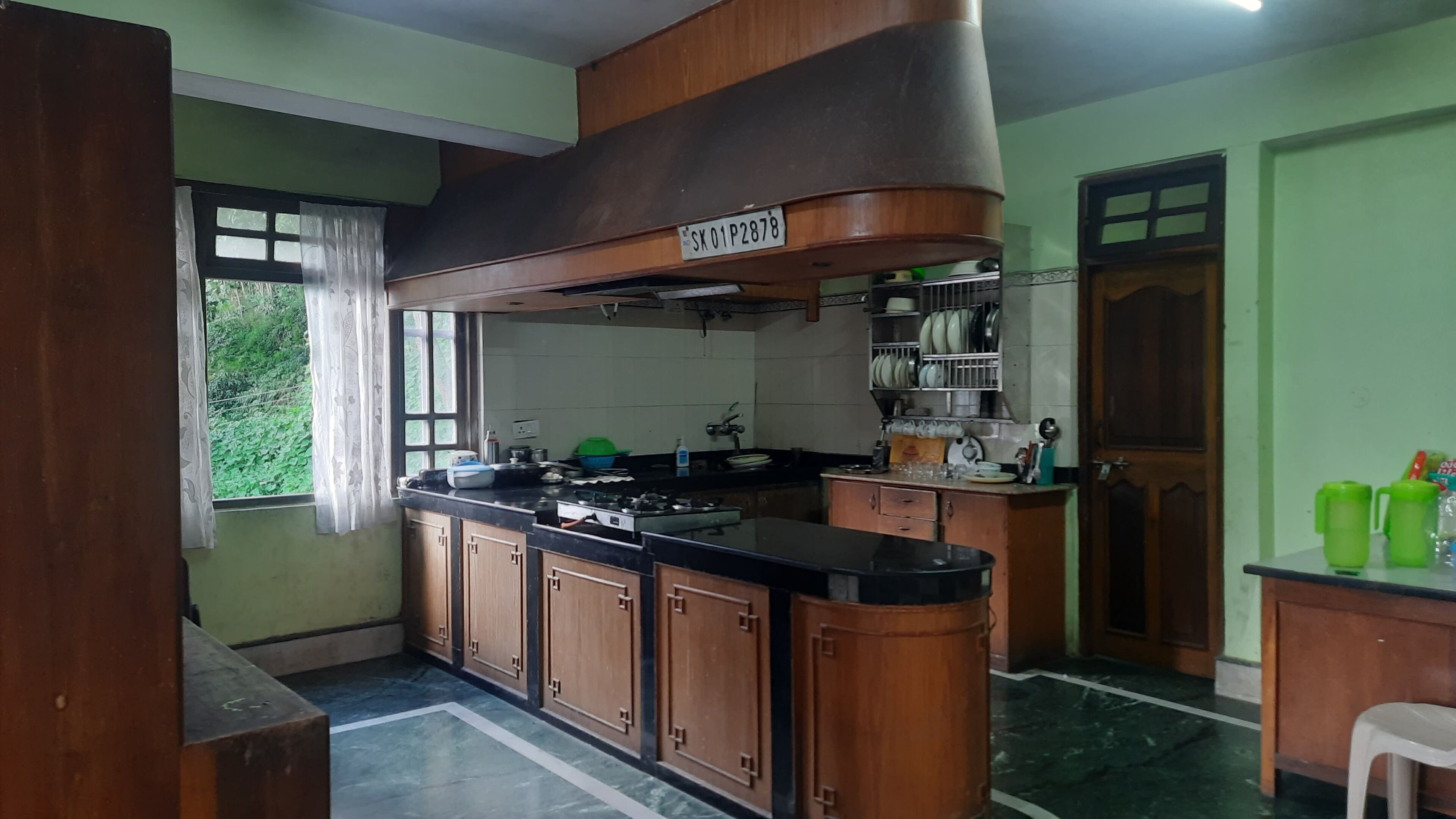 A kitchen with wooden cabinets, a black countertop, and a stove. There is a window with a curtain, a sink, and a dish rack.