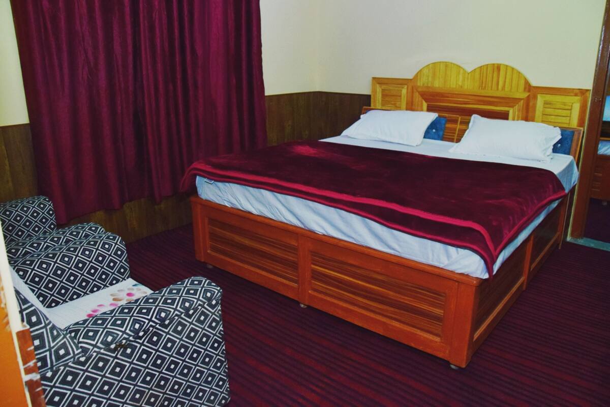 A hotel room with a wooden bed, a red curtain, and a patterned chair.