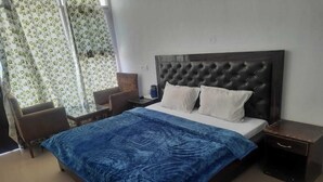 A bedroom with a large bed, two pillows, a blue bedspread, a wooden headboard, a nightstand, a chair, and a window with curtains. - Snow View Homestay (Sainj)