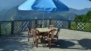 A table with chairs and a blue umbrella under a mountain view. - Snow View Homestay (Sainj)