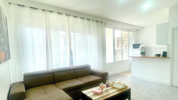 A living room with a brown sofa, a wooden coffee table, and a kitchen area in the background. - Spacious and bright, a real "coup de coeur" near the metro and RER station (La Courneuve)