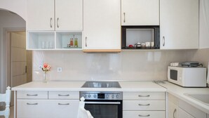 A kitchen with white cabinets, a built-in oven, a microwave, and a small shelf with kitchen items. - Anna Maria Family House#1 (Kalampaka)