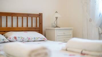 A bedroom with a wooden headboard, a bedside table with a lamp, a white dresser, and a bed with floral bedding.