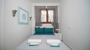 A bedroom with a bed, two pillows, a nightstand, a lamp, and a window with curtains. - Anna Maria Family House#1 (Kalampaka)