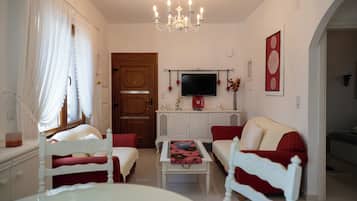 Una stanza ben illuminata con un lampadario, una televisione montata a parete e un divano rosso e bianco.
