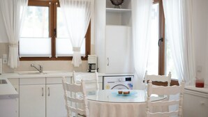 A kitchen with white cabinets, a sink, and a coffee machine. There is a round table with two chairs and a glass top. - Anna Maria Family House#1 (Kalampaka)