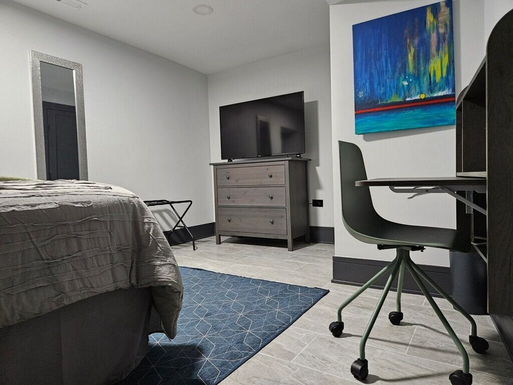 Un dormitorio moderno con cama, escritorio, silla, cómoda y televisor.