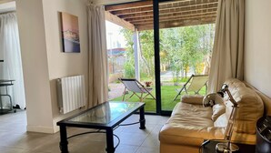 A living room with a glass-top coffee table, a leather sofa, and a view of a garden through a sliding glass door.