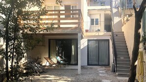 A residential building with a covered patio, a staircase, and a gravel driveway.