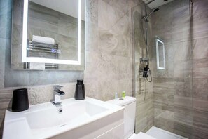 A modern bathroom with a large mirror, a white sink, a shower enclosure, and a towel rack. - The Cove - Roker Sea Front - Vacant Nests (Roker)