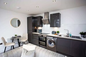 A modern kitchen with dark cabinetry, a built-in oven, a washing machine, and a round mirror on the wall.