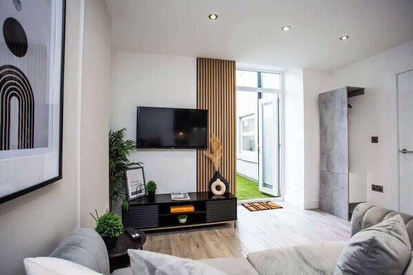 A modern living room with a flat-screen TV, a wooden accent wall, and a large window.