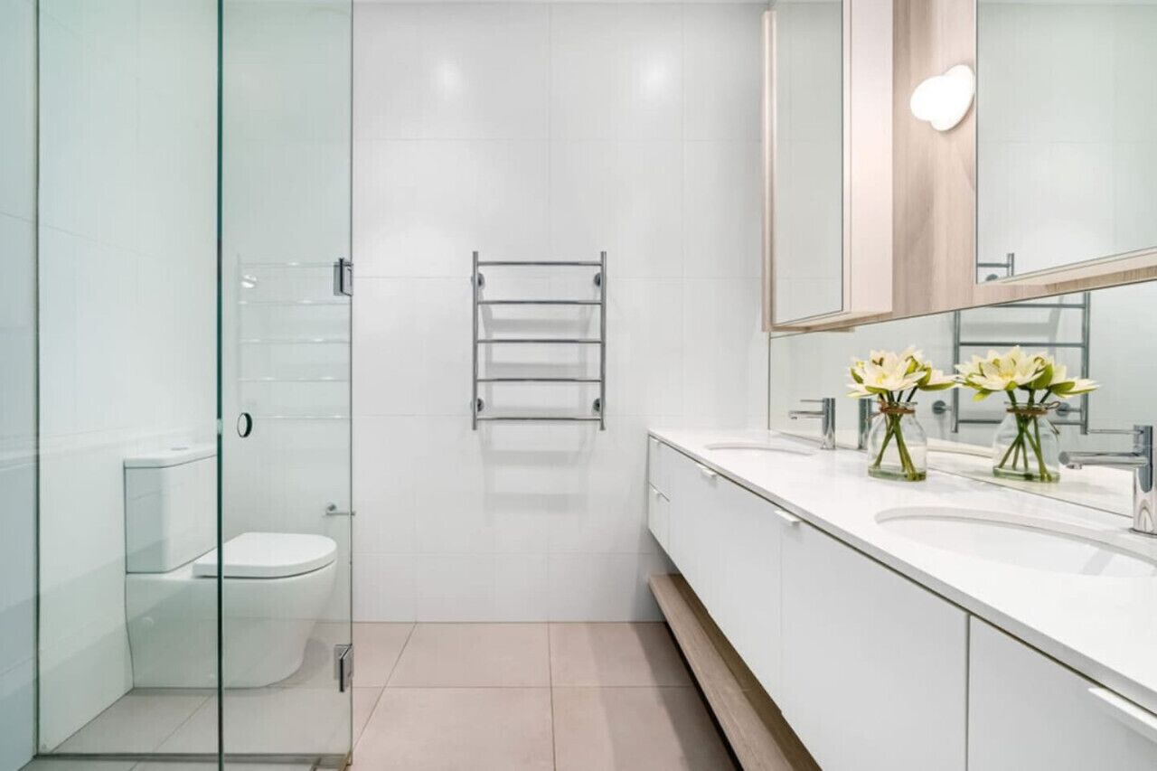 A modern bathroom with a glass shower enclosure, a white toilet, a towel rack, and a vanity with a mirror and two flower vases.