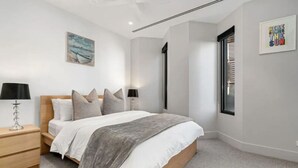 A modern bedroom with a wooden bed, a nightstand, a lamp, and a window with blinds. - Anchors Away | Escape in the heart of Mornington (Mornington)