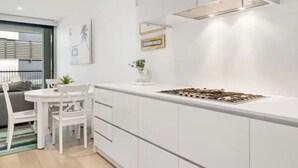 A modern kitchen with white cabinetry, a gas stove, and a small dining area with a white table and chairs. - Anchors Away | Escape in the heart of Mornington (Mornington)