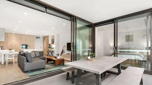 A modern living room with a grey sofa, a dining table, and a glass partition. - Anchors Away | Escape in the heart of Mornington (Mornington)