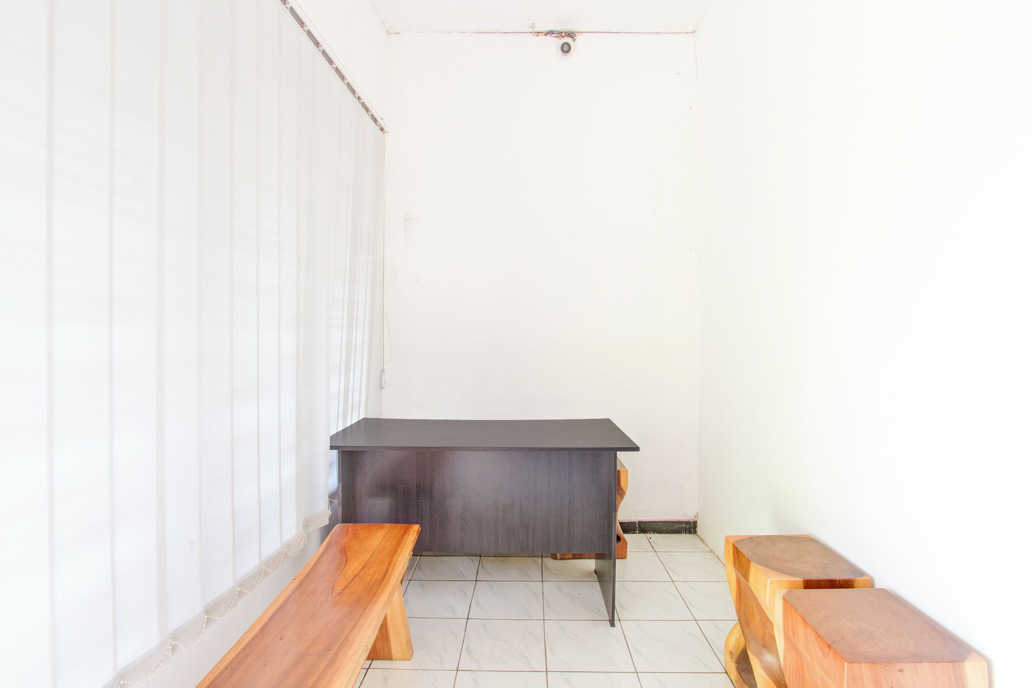A room with a dark wooden desk, two wooden benches, and a white wall.
