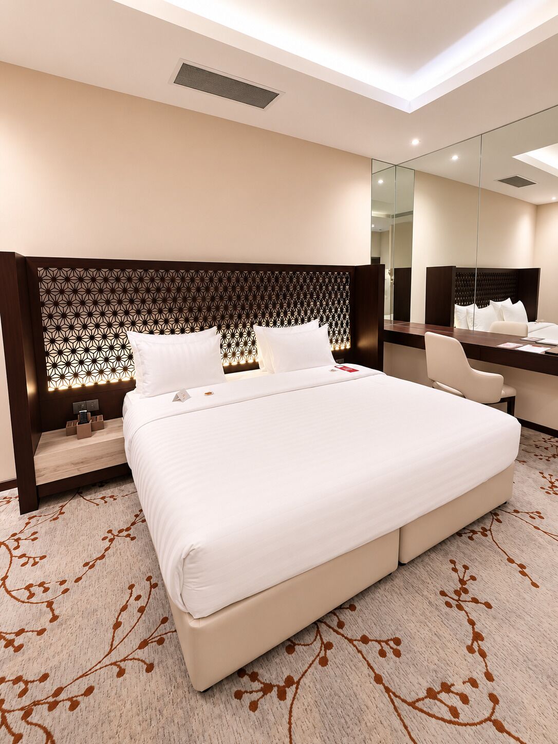 A modern hotel room with a large bed, a desk, and a mirror.