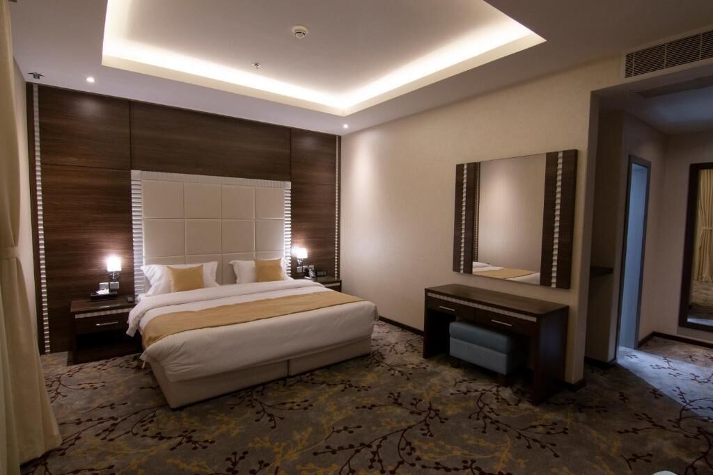 A hotel room with a large bed, a desk, a mirror, and a ceiling light.