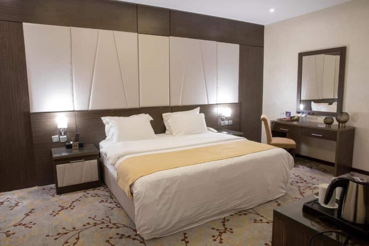 Quarto de hotel com cama grande, mesas de cabeceira, cômoda, espelho e cafeteira.