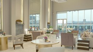 A spacious, modern lounge area with comfortable seating, a central round table, and large windows offering a city view. - Ayan Hotel (Riyadh)