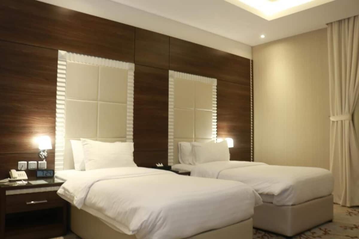 Quarto de hotel com duas camas, uma mesinha de cabeceira com abajur e um espelho grande.