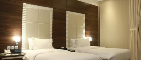 A hotel room with two beds, a nightstand with a lamp, and a large mirror.