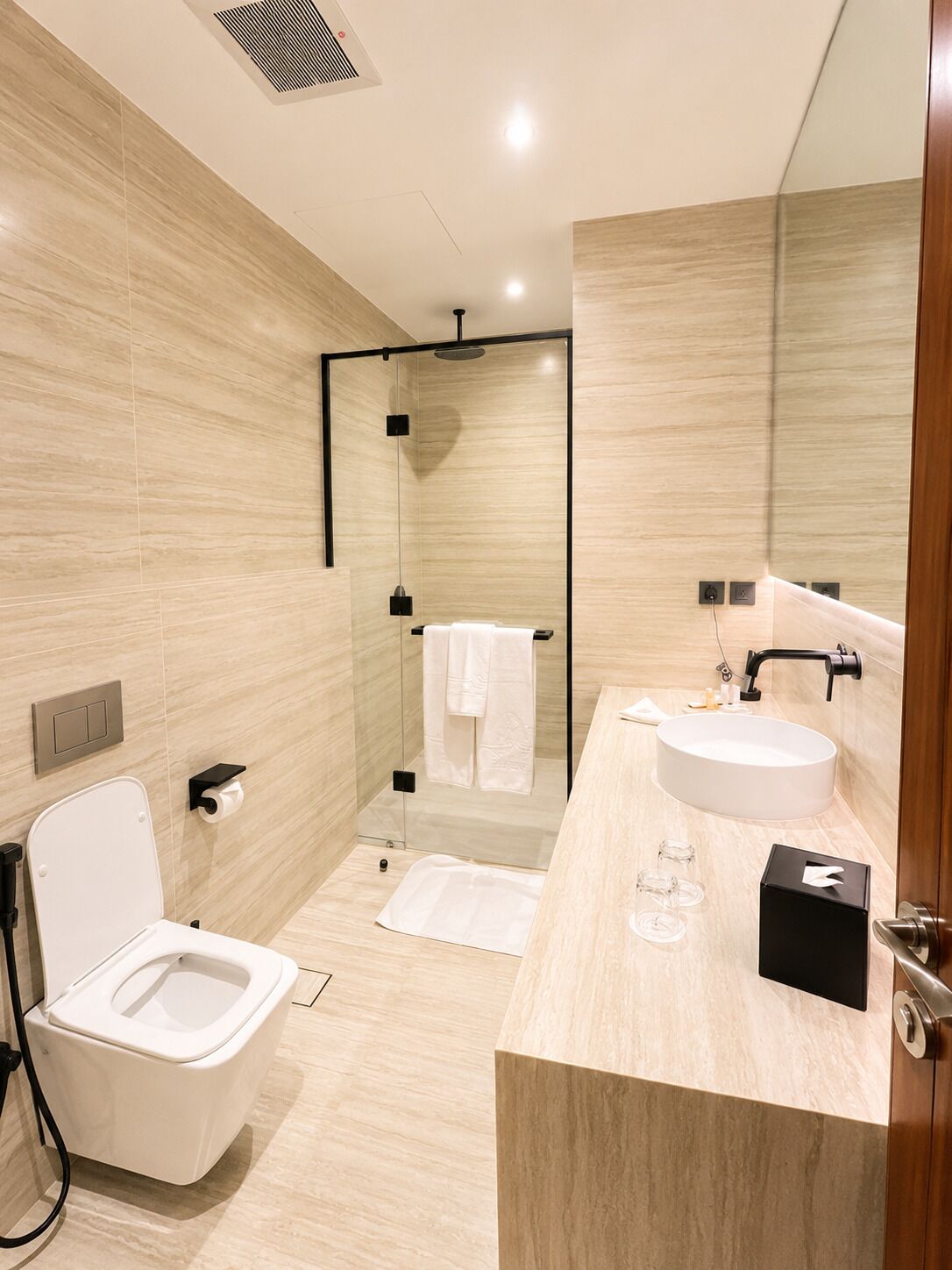 A modern bathroom with a toilet, bidet, sink, and a glass shower enclosure.