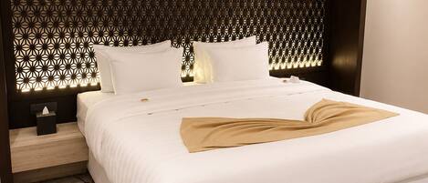 Habitación de hotel con una cama grande, cabecera con diseño geométrico, mesita de noche con lámpara y alfombra floral.